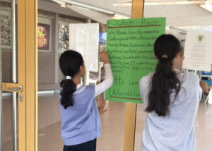Schülerinnen hängen selbstgemachte Plakate in der Schule auf
